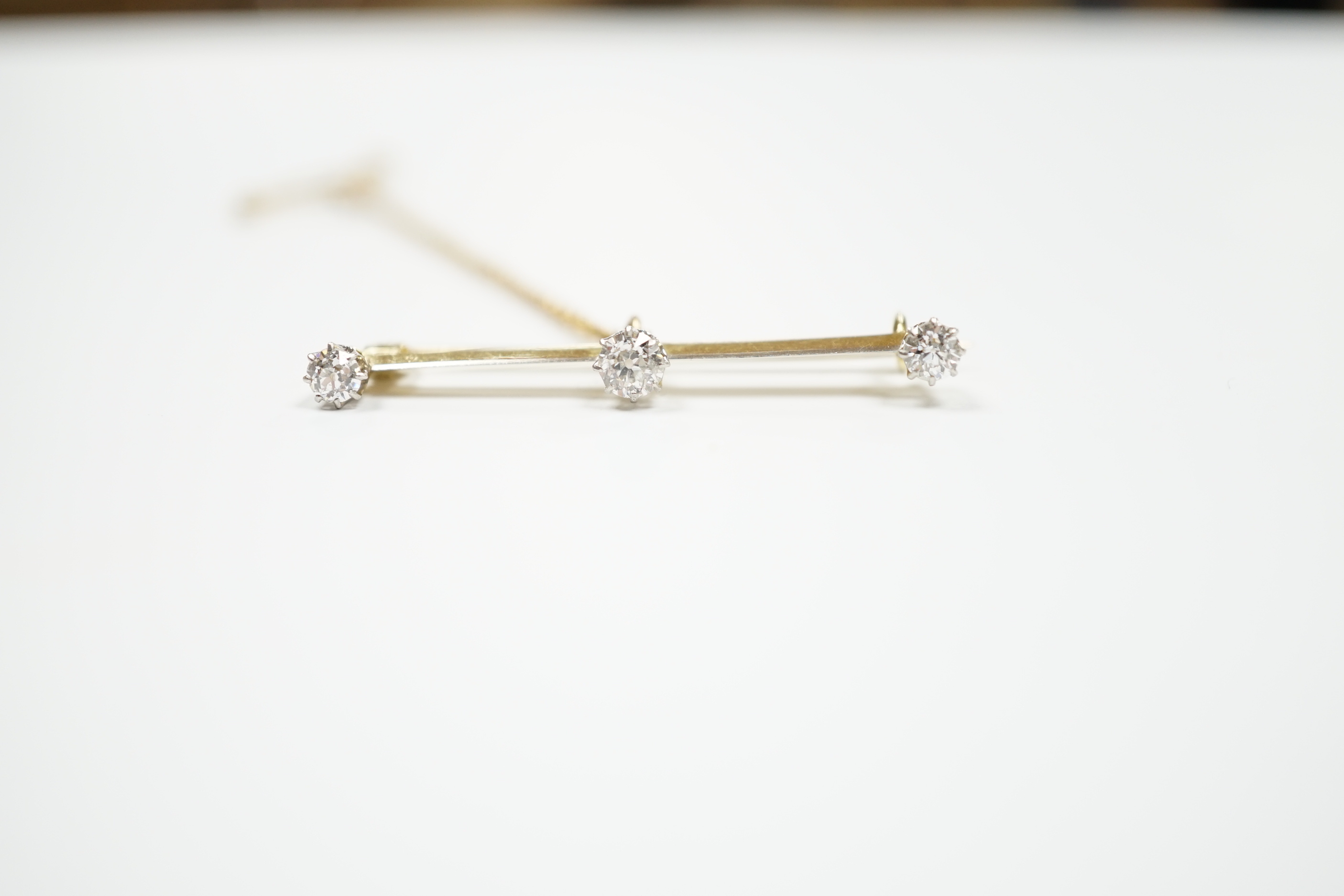 A yellow metal and three stone diamond set bar brooch, 37mm, with safety chain, gross weight 3 grams.